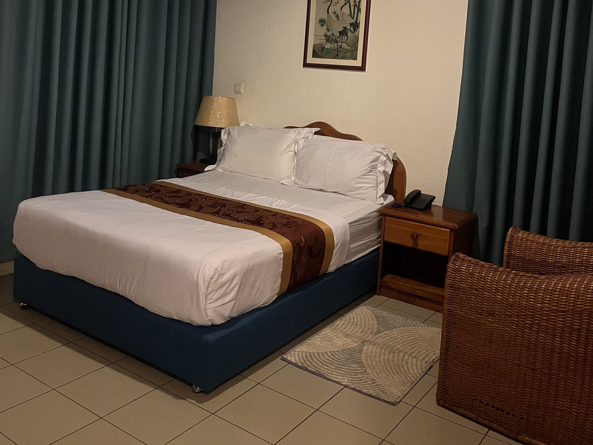 Standard room with one double bed, teal curtains and a wicker armchair